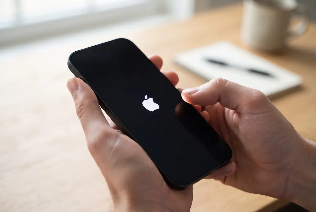 Thumb pressing the side button of an iPhone that shows the Apple logo while it restarts